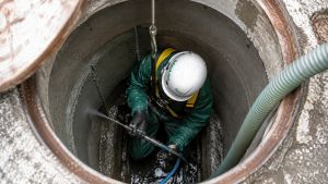 Tecnico Ideal-Jet all'interno di un pozzetto d'ispezione durante il risanamento e l'impermeabilizzazione delle pareti con malte cementizie impermeabili per reti fognarie.